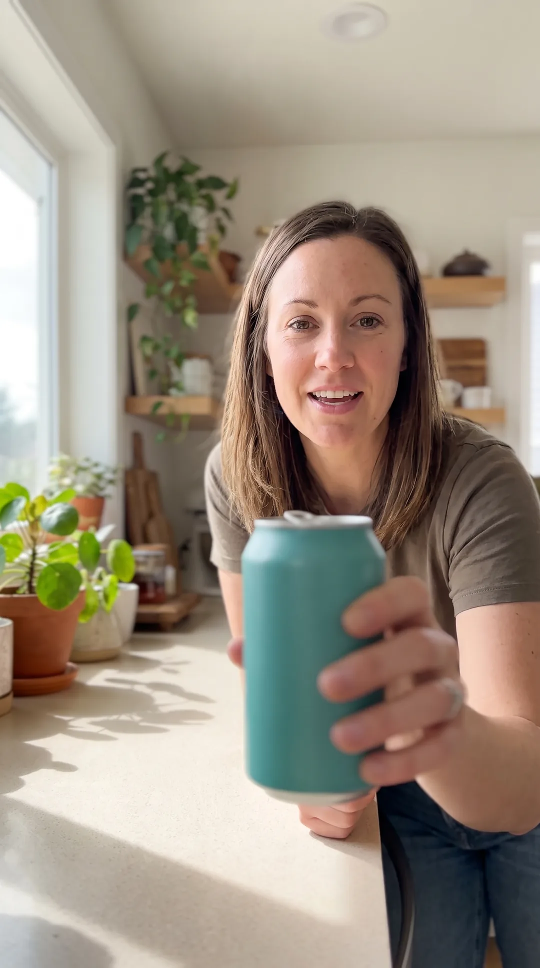 A creator holding an unbranded drink can to camera in a sunlit kitchen